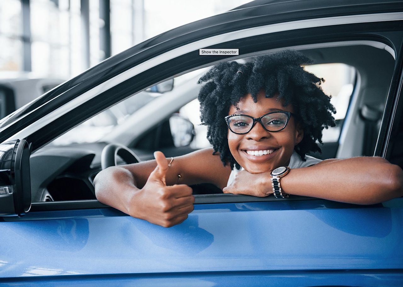 Shows thumb up. Young african american woman sits inside of new modern car by mstandret